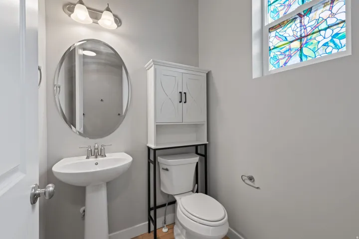Pedestal sink with a brushed nickel faucet, oval mirror, and a stained-glass window