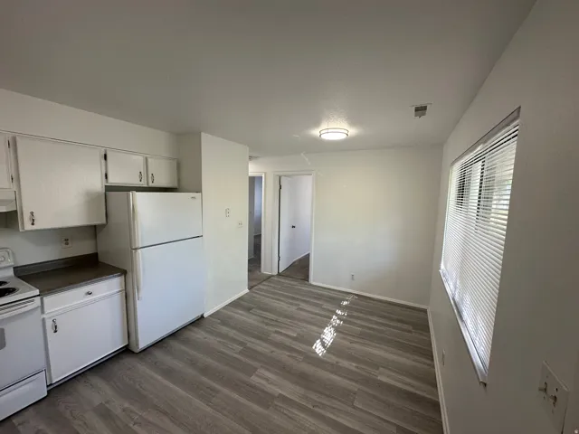 Kitchen and dining area featuring wood-finish flooring, white cabinetry, and white appliances including a refrigerator and electric range