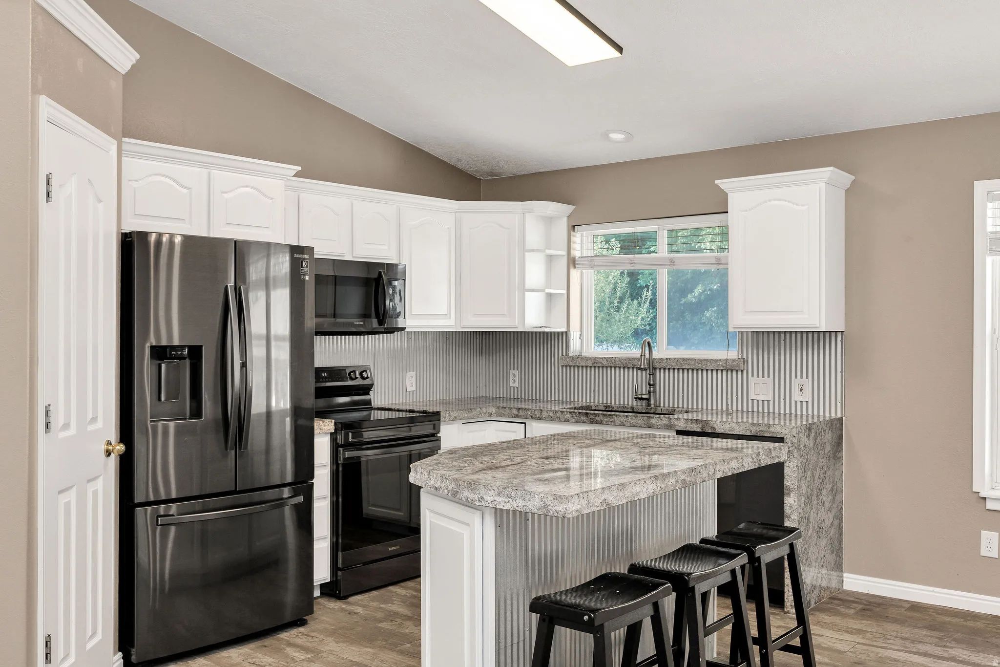 Kitchen featuring white cabinetry, dark stainless steel appliances, a breakfast bar, wood-finish flooring, and a corrugated metal backsplash