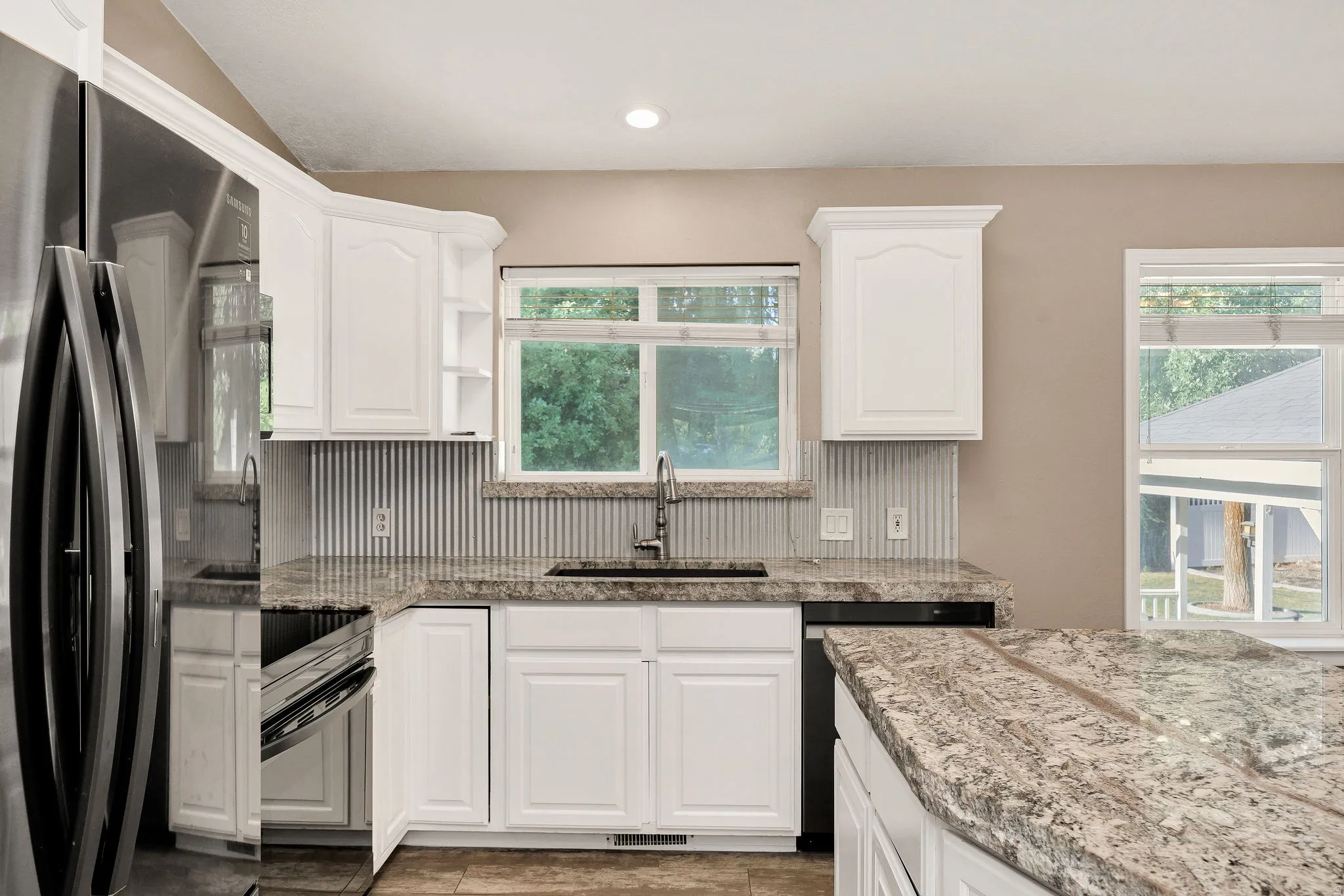 Kitchen with white cabinetry, granite countertops, and a corrugated metal backsplash