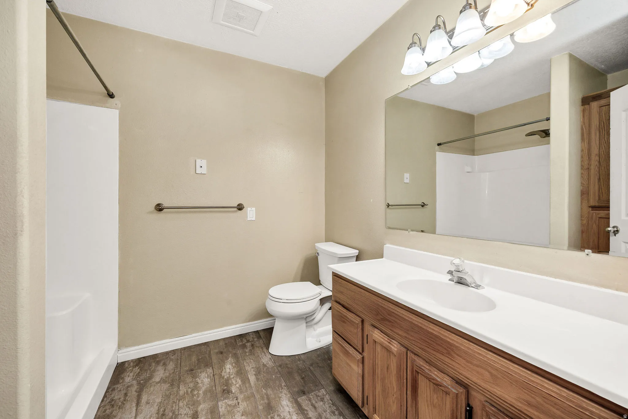 Bathroom featuring a wood-finish vanity with a white countertop and integrated sink, a large wall-mounted mirror, and a combination tub/shower