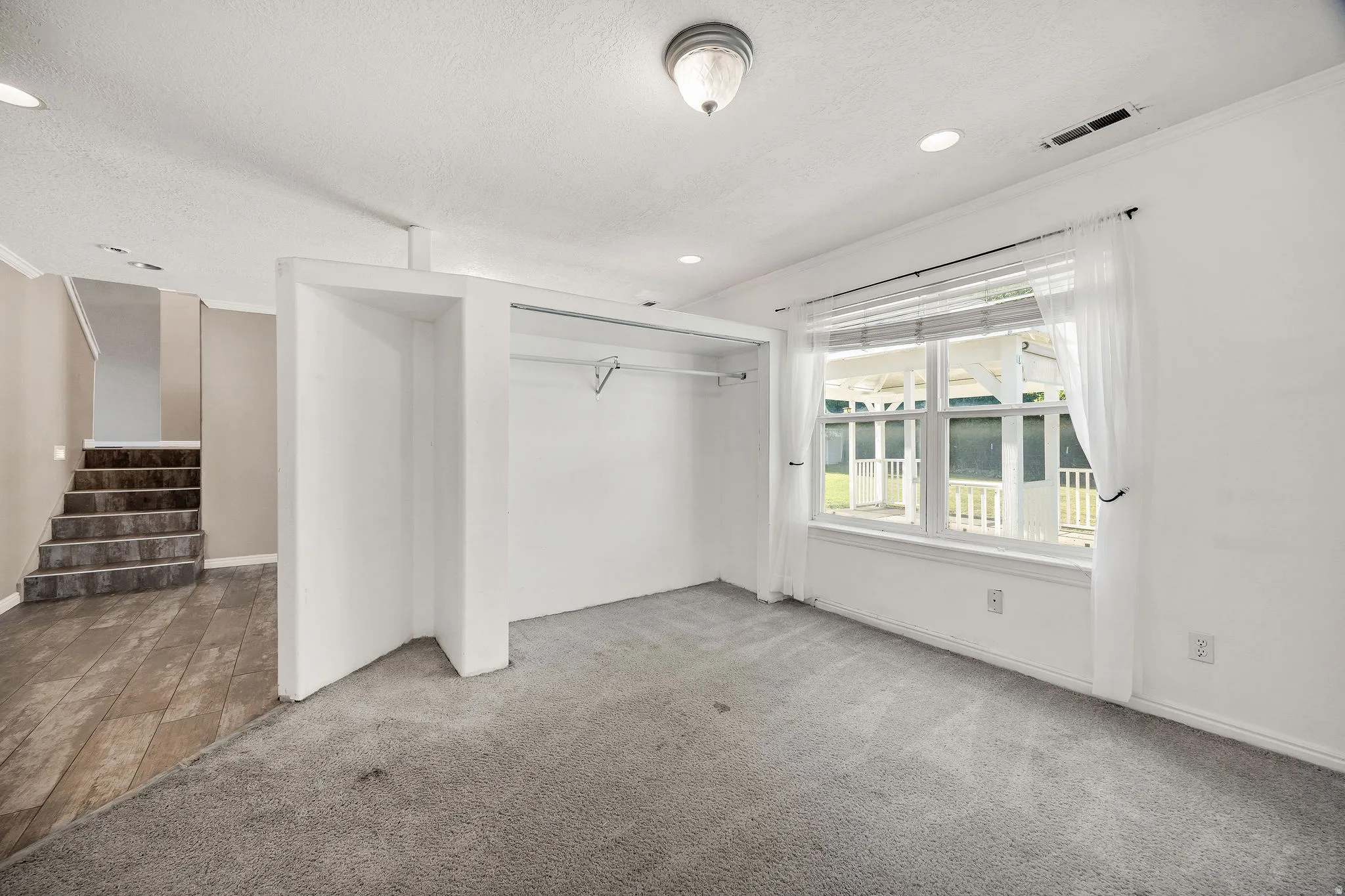 Bright room featuring neutral carpeting, a large window, recessed lighting, and an open closet space