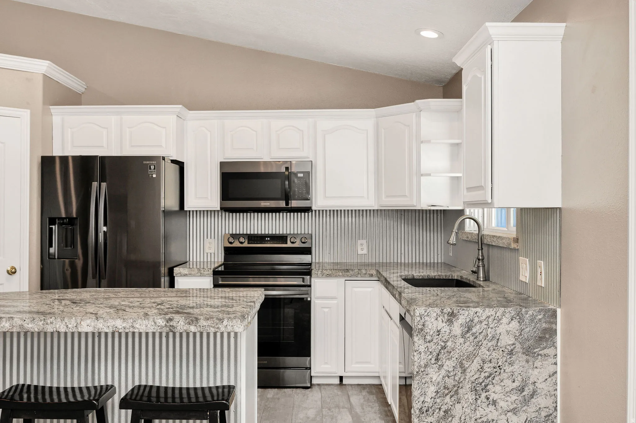Kitchen featuring white cabinetry, stone countertops, stainless steel appliances, a bar seating area, and wood-finish flooring