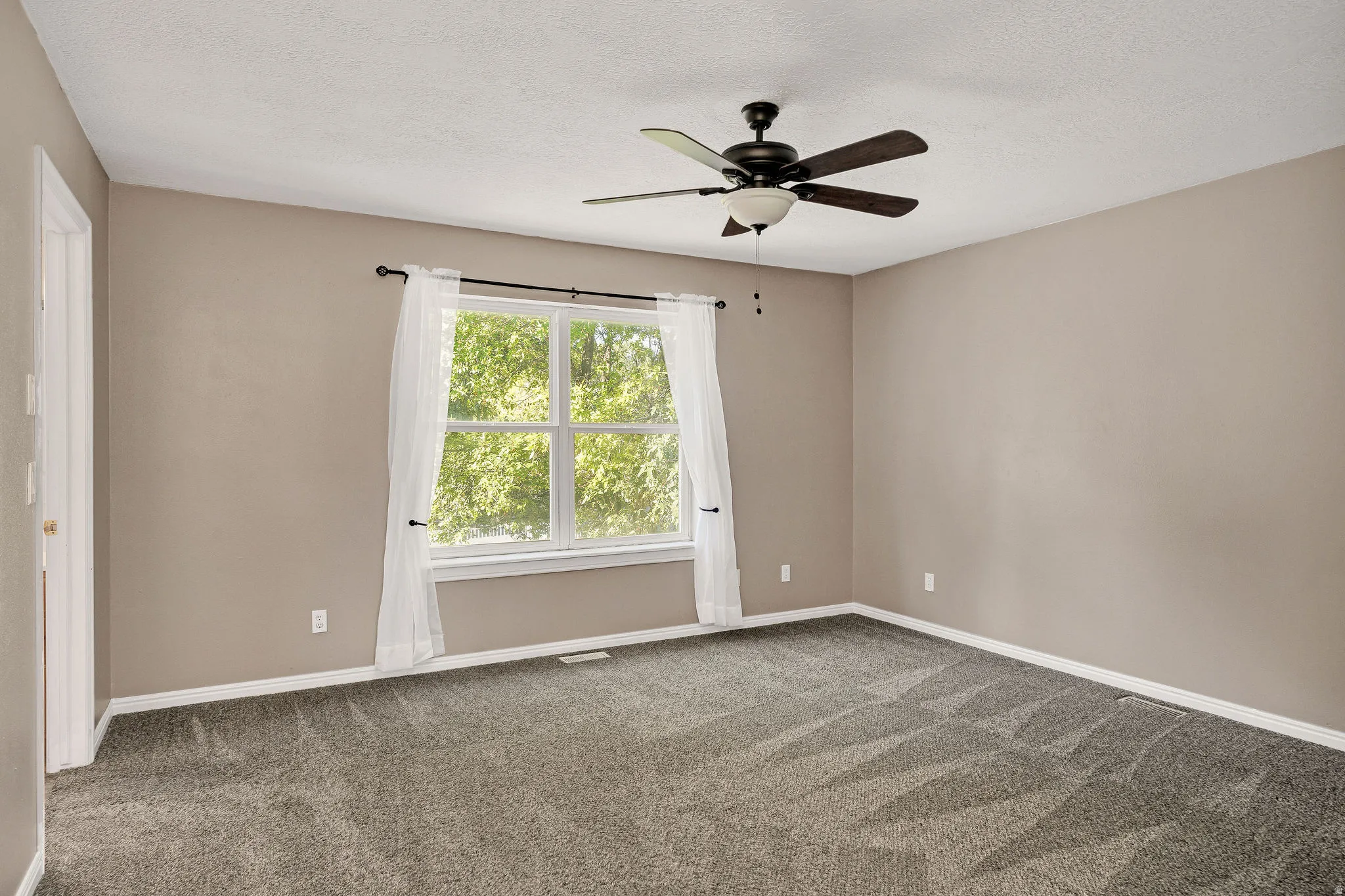 Spacious room featuring neutral-toned walls, a large window, and gray patterned carpeting