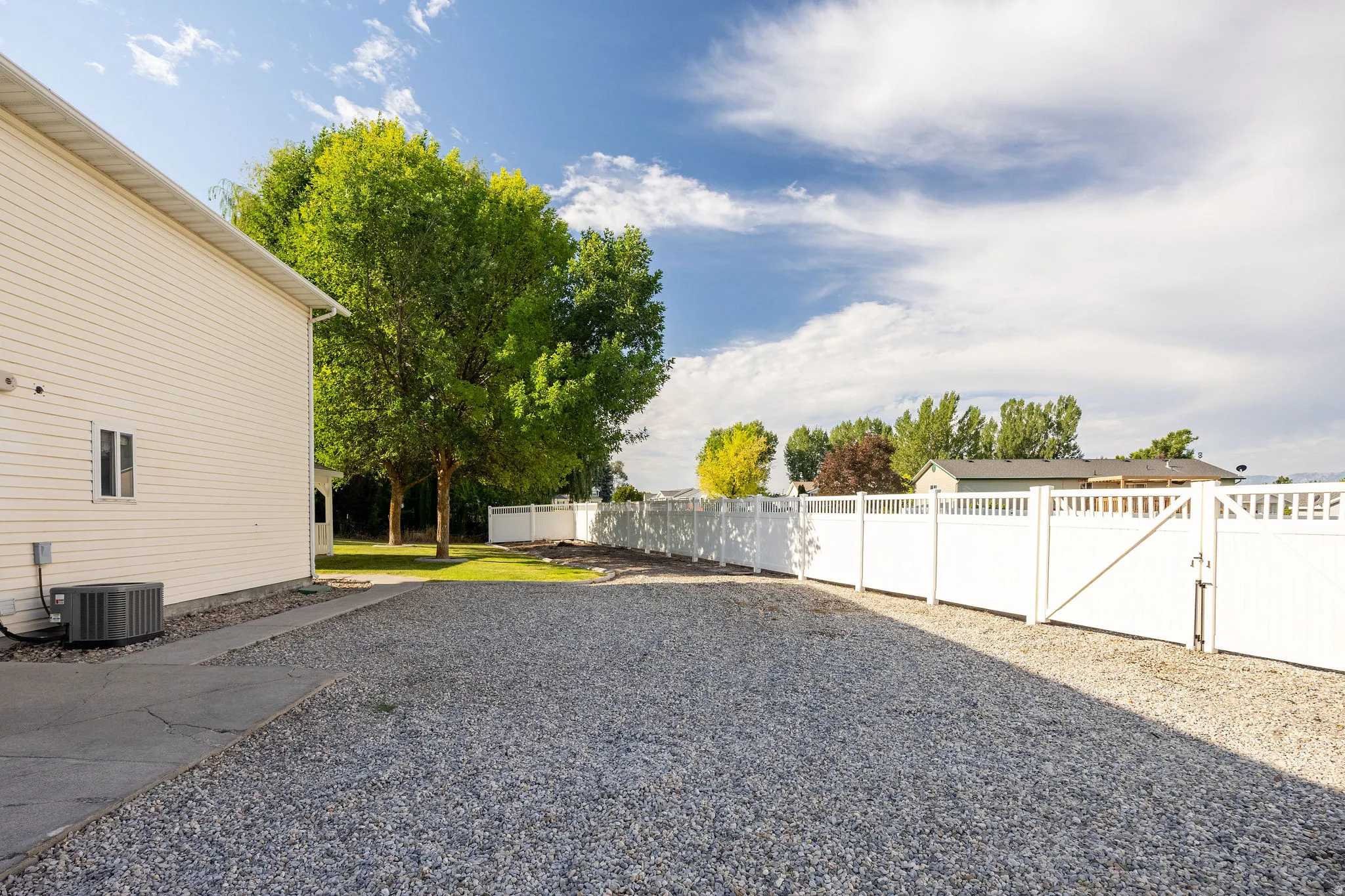 Gravel driveway with a partial white vinyl fence and gate