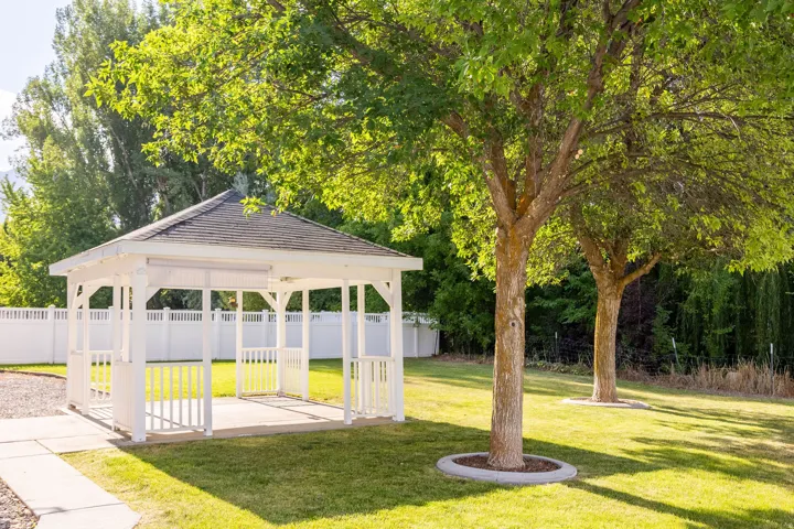 White gazebo with a dark shingled roof, set on a concrete pad with an adjacent paved pathway