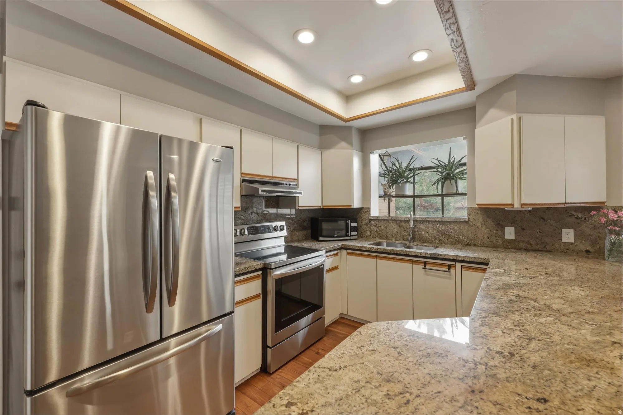 Kitchen featuring stainless steel appliances, light cabinetry, granite countertops, and wood-finish flooring