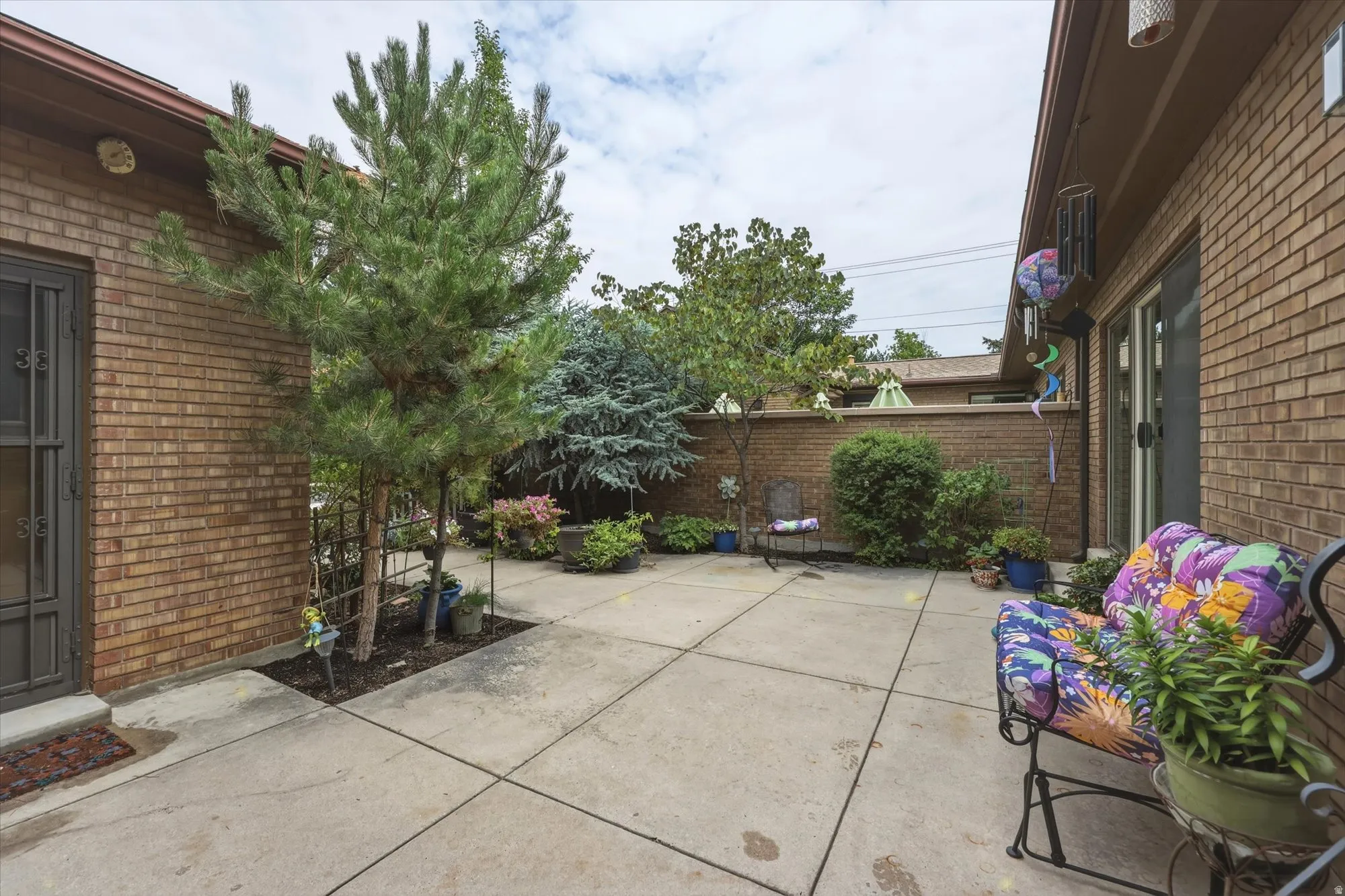 Private patio featuring concrete surfacing, brick exterior walls, mature plantings, and direct entry points