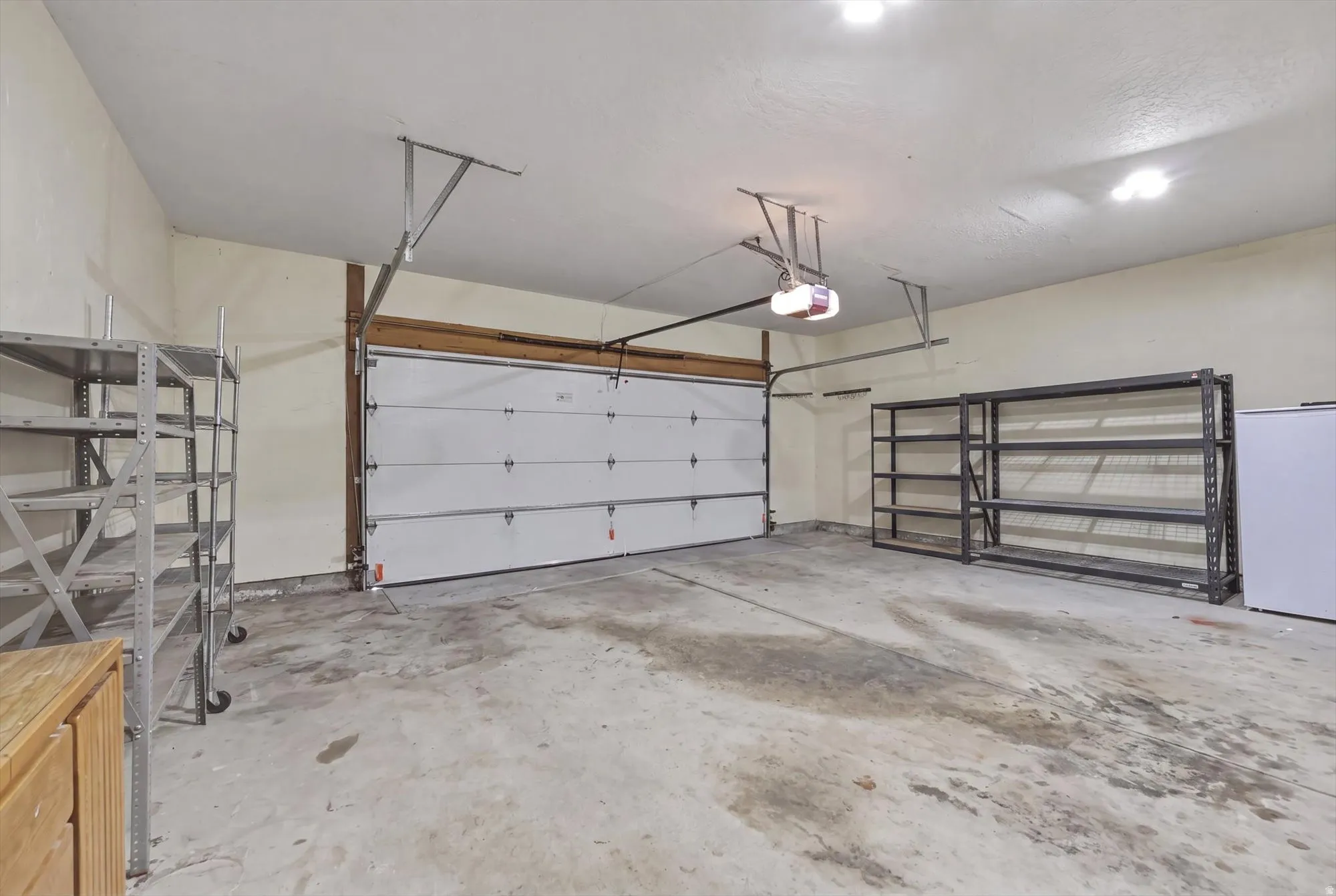 Spacious garage with a white sectional door, exposed wooden header, overhead lighting, and an automatic garage door opener