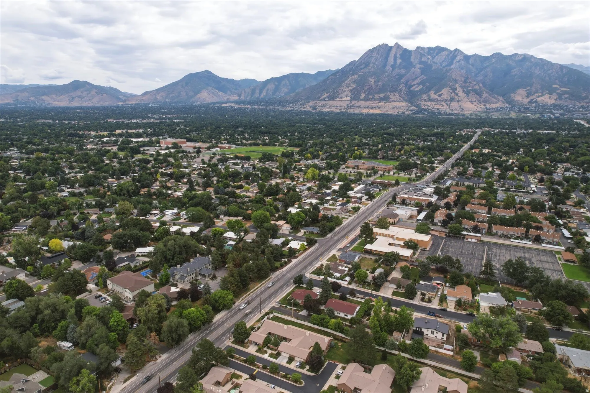 Expansive aerial panorama showcasing a residential area with extensive tree coverage and a prominent roadway
