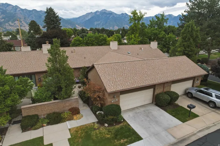 Brick exterior with a brown shingle roof, featuring attached dual-car garages, a concrete driveway, and mature landscaping
