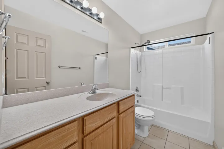Bathroom featuring a light wood-finish vanity with an integrated sink, a large wall-mounted mirror, overhead vanity lighting, and a bathtub with an integrated shower and window