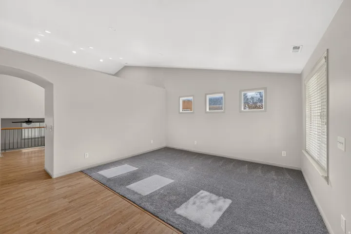 Vaulted ceiling, recessed lighting, wood-finish flooring, grey carpeting, multiple windows with blinds