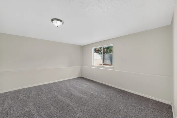 Neutral-toned walls with a white trim, featuring a window and a ceiling-mounted light fixture, over a textured gray carpet