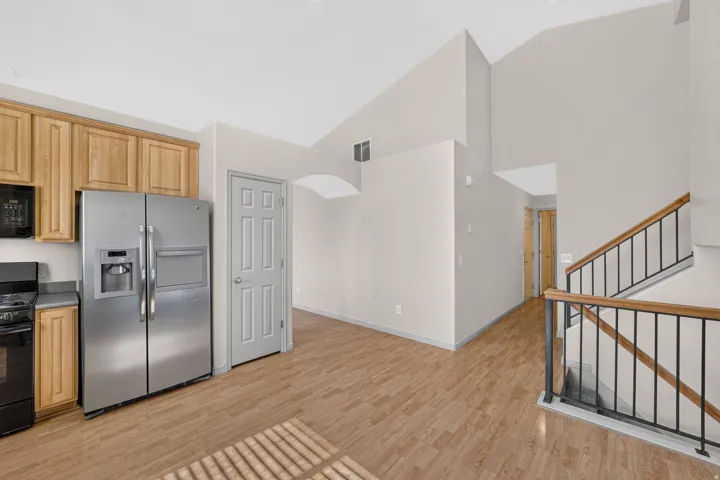 Wood-finish flooring throughout, vaulted ceiling, wood cabinetry, stainless steel side-by-side refrigerator, and a modern stair railing