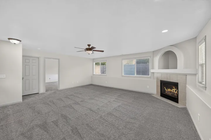 Spacious room featuring neutral carpeting, a corner fireplace with tiled surround, a built-in arched alcove, and a ceiling fan