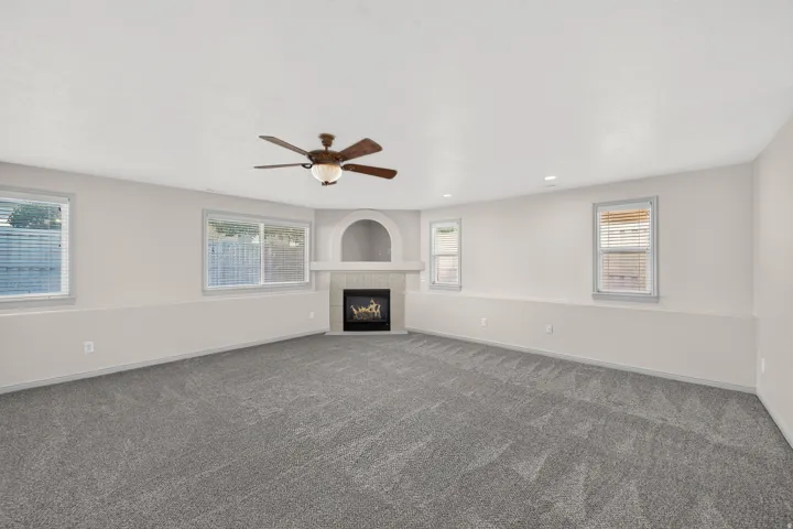 Spacious room featuring gray carpeting, multiple windows with blinds, a built-in fireplace with an arched niche, and a ceiling fan