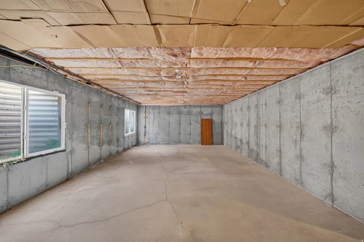 Unfinished basement featuring concrete walls and flooring, two windows, and exposed ceiling joists