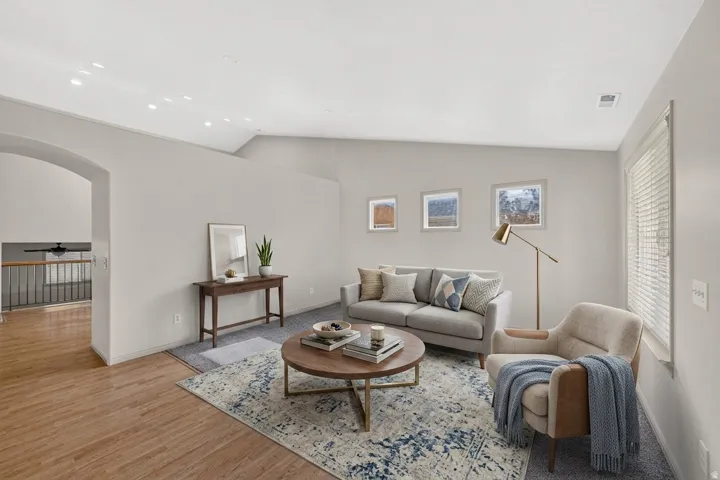 Living area featuring a vaulted ceiling with recessed lighting, wood-finish flooring, and ample natural light from a large window