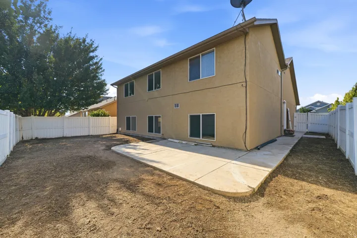 Stucco exterior with multiple windows, concrete patio, and white privacy fencing