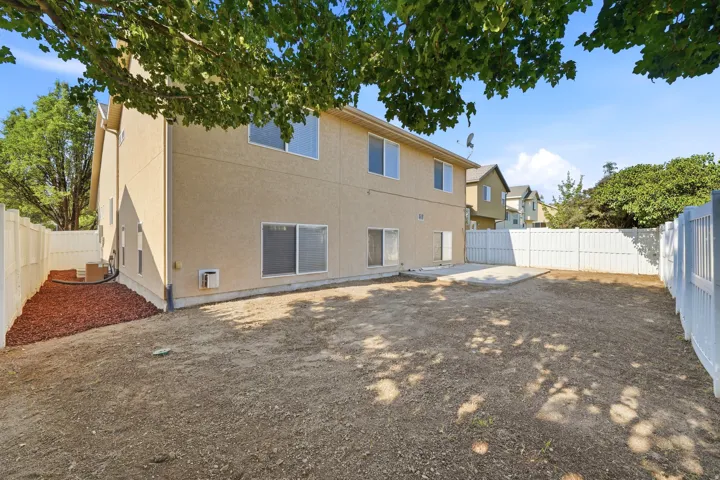 Expansive backyard with a concrete patio, white privacy fencing, and a mulched area