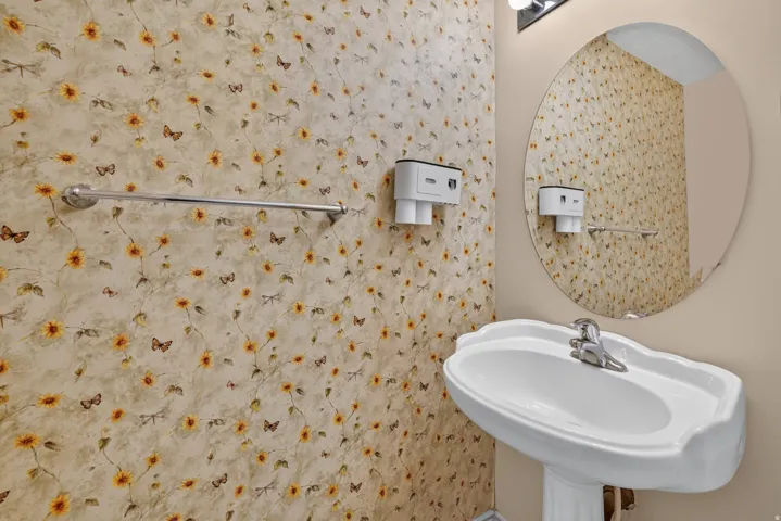 Pedestal sink with chrome faucet, oval mirror, and wall-mounted light fixture