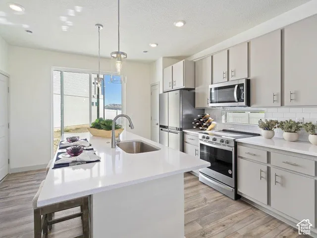Modern kitchen featuring a large island with an undermount sink, stainless steel appliances, light cabinetry, white countertops, and wood-finish flooring
