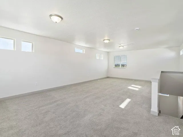 Spacious carpeted room featuring multiple windows, flush-mount ceiling lights, and a white painted railing