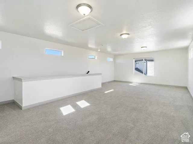 Spacious open room featuring light gray carpet, multiple flush-mount ceiling lights, a half-wall partition, and rectangular windows