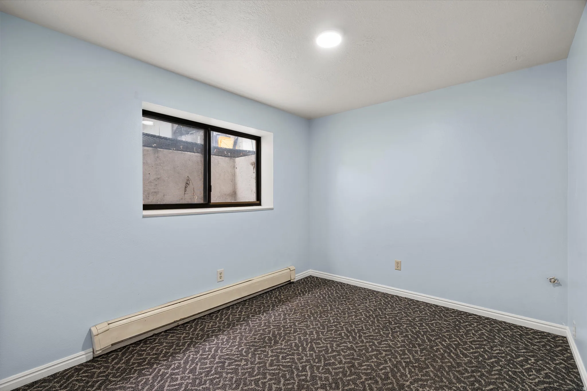 Room featuring a neutral wall color, patterned carpet flooring, a window with a black frame, and a baseboard heater