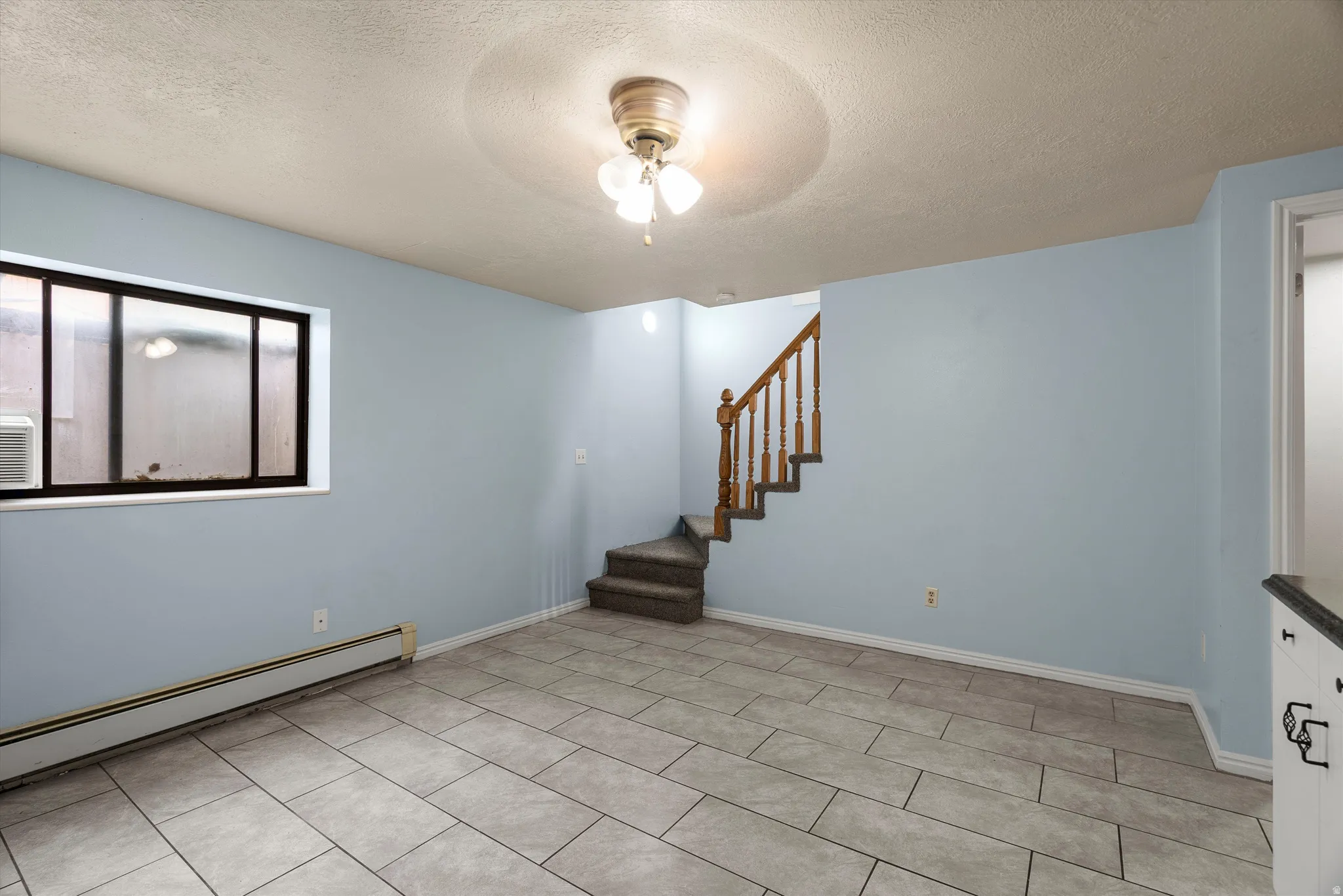 Spacious room featuring light blue walls, rectangular tile flooring, and a window with a black frame