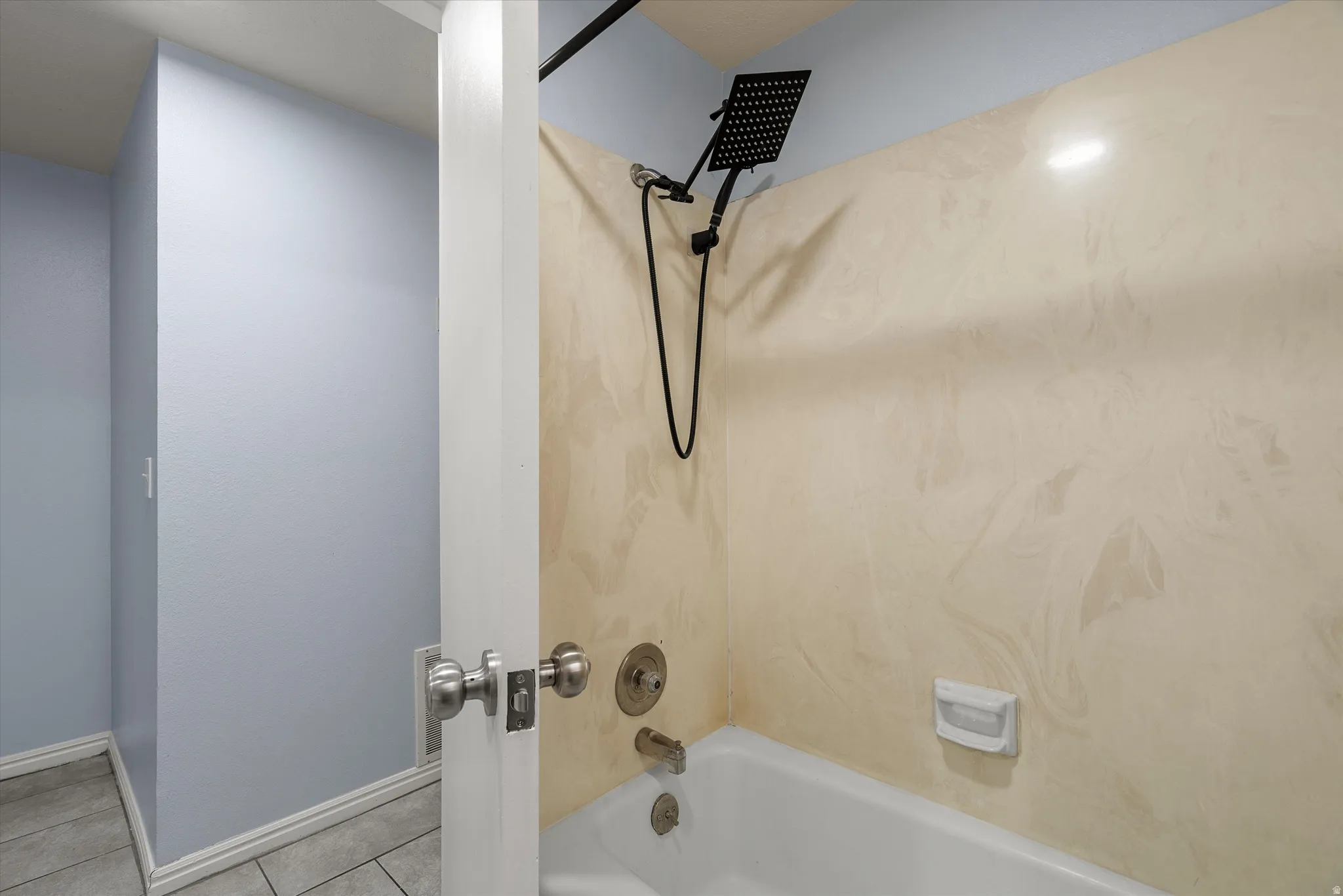 Bathtub with a black rainfall showerhead, brushed nickel fixtures, and a light-toned, subtly patterned surround