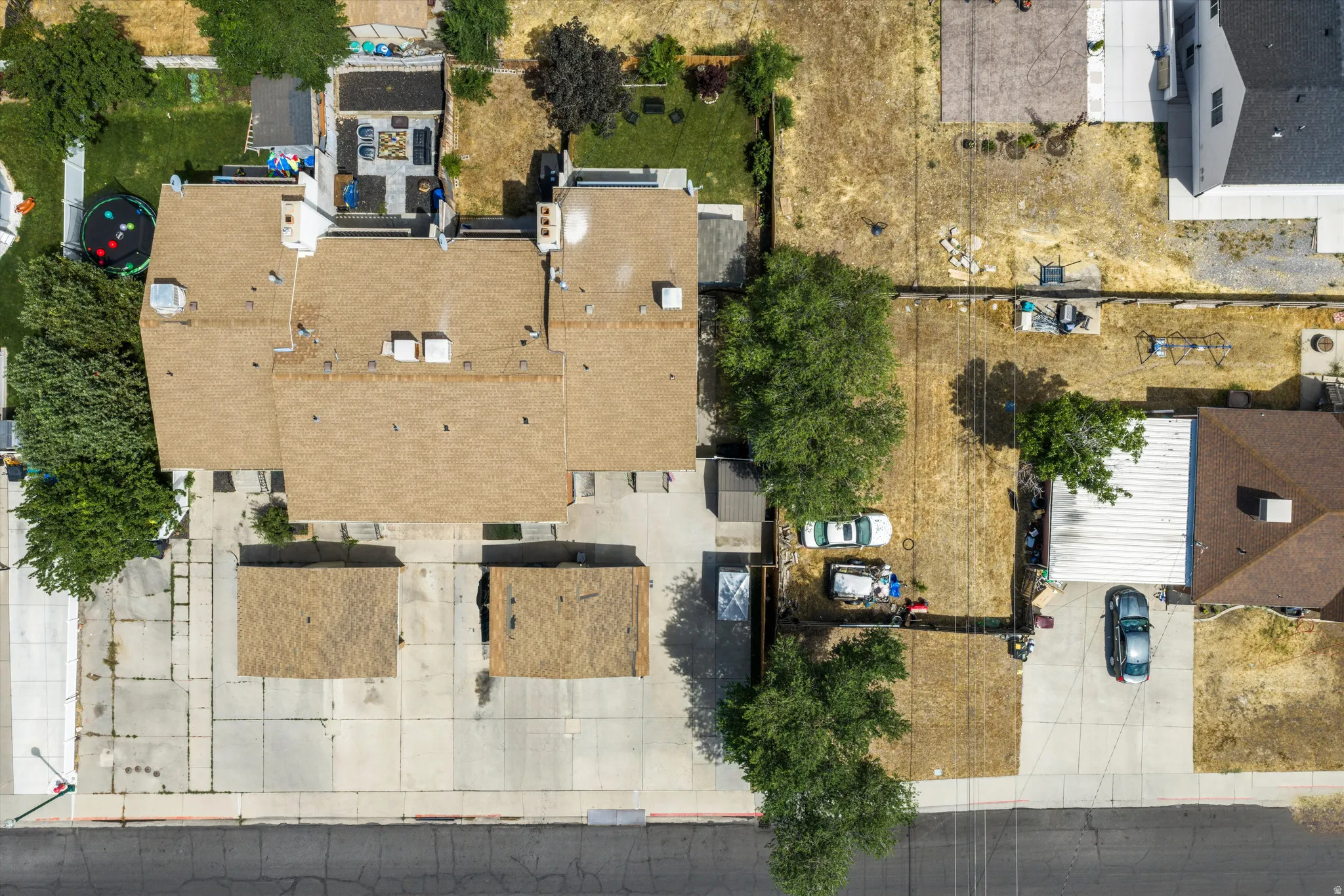 Property featuring a large residential structure with a brown shingle roof, two detached garages with matching shingle roofs, and extensive concrete paving