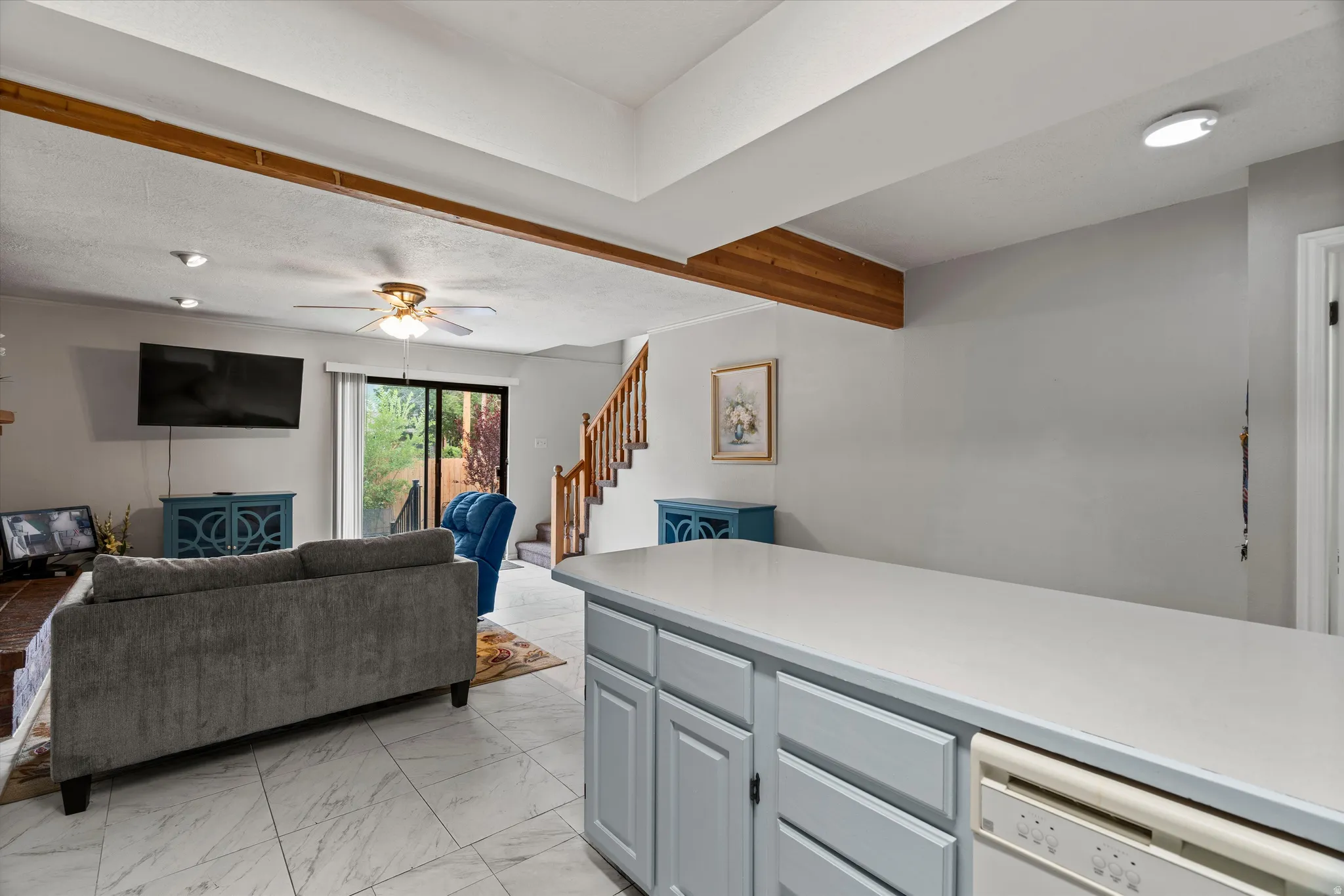 Open-concept living space featuring wood-finish ceiling beams, large format tile flooring, and a sliding glass door leading to exterior space