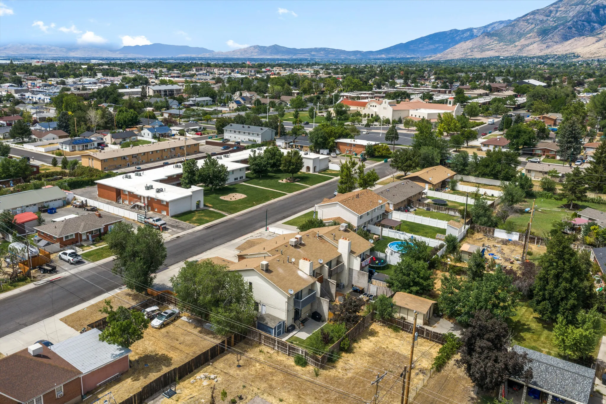 Aerial view showcasing a residential neighborhood with established homes, mature trees, and a distant mountain range backdrop