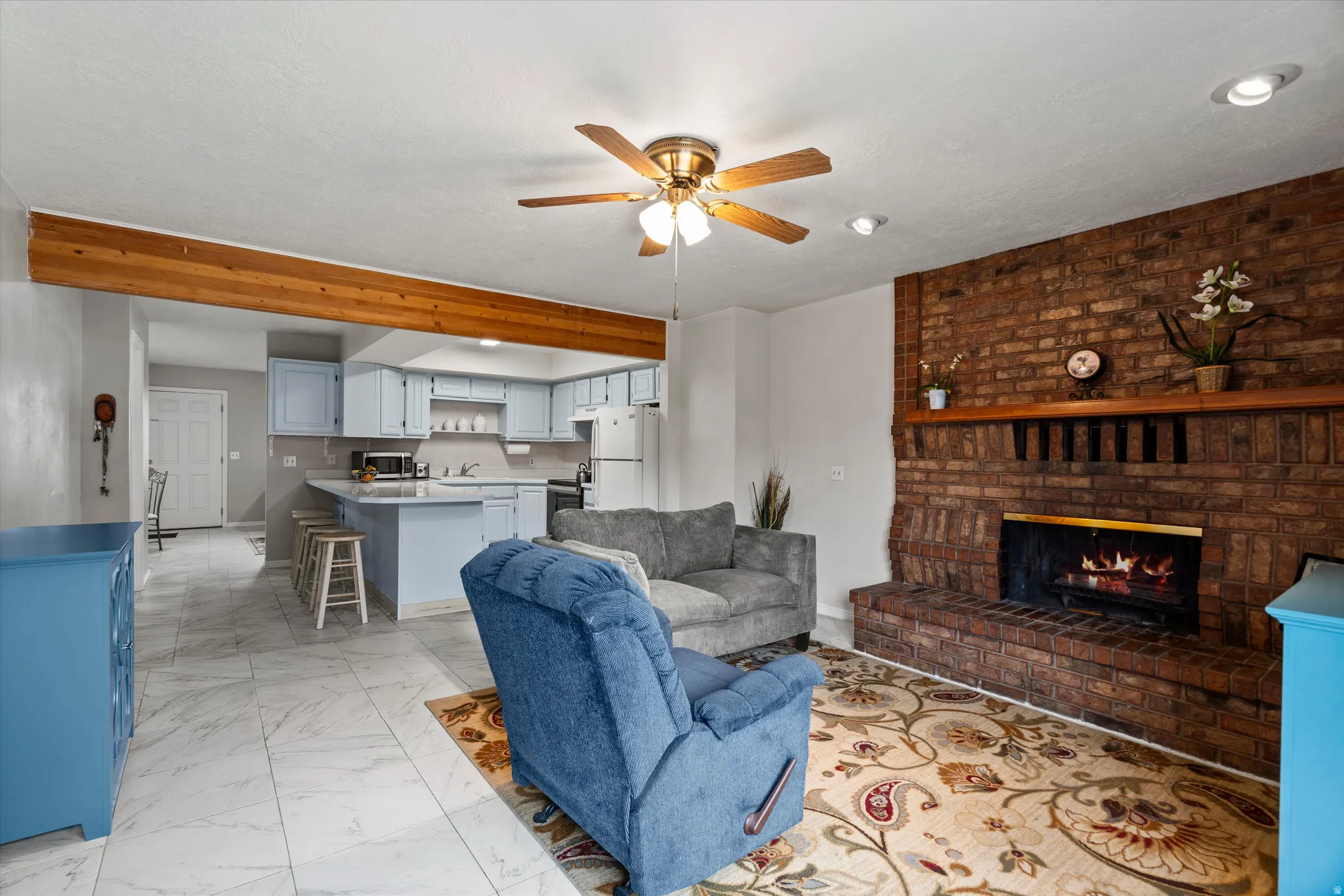 Spacious living area featuring a brick fireplace, wood mantel, and ceiling fan
