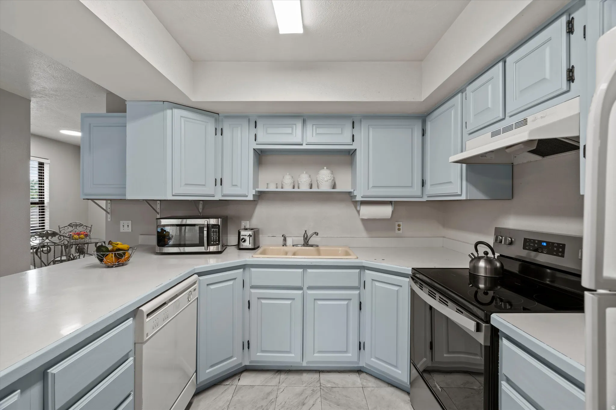 U-shaped kitchen featuring light blue cabinetry, solid surface countertops, a white built-in dishwasher, a black and stainless steel range, and tile flooring