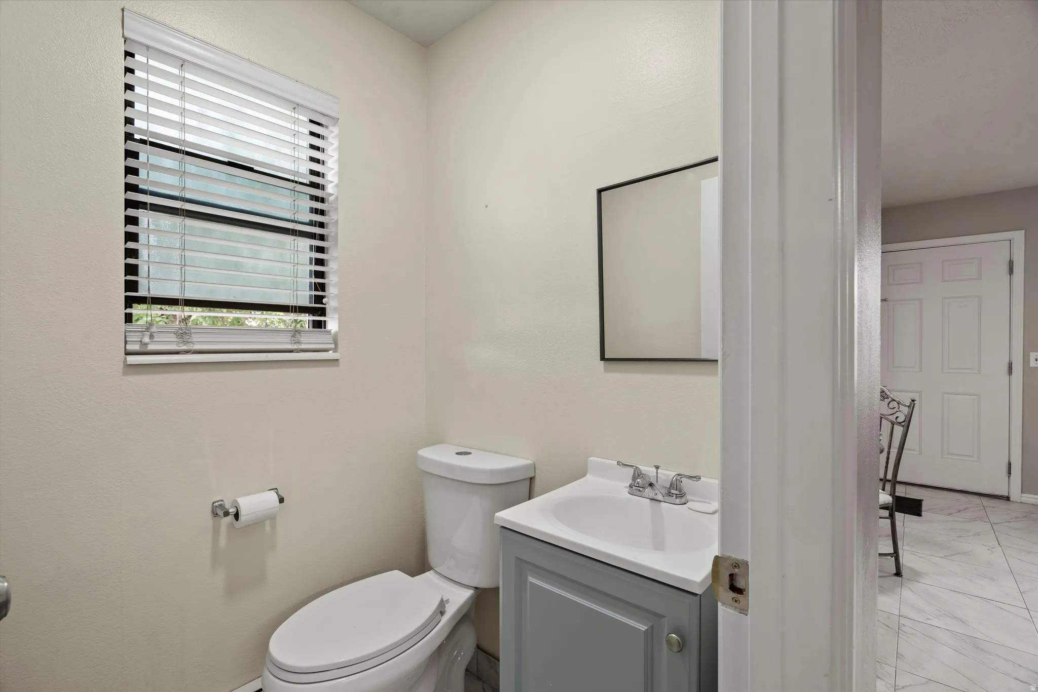 Half bathroom featuring a single window with blinds, a vanity with a grey cabinet and white countertop, and a white toilet