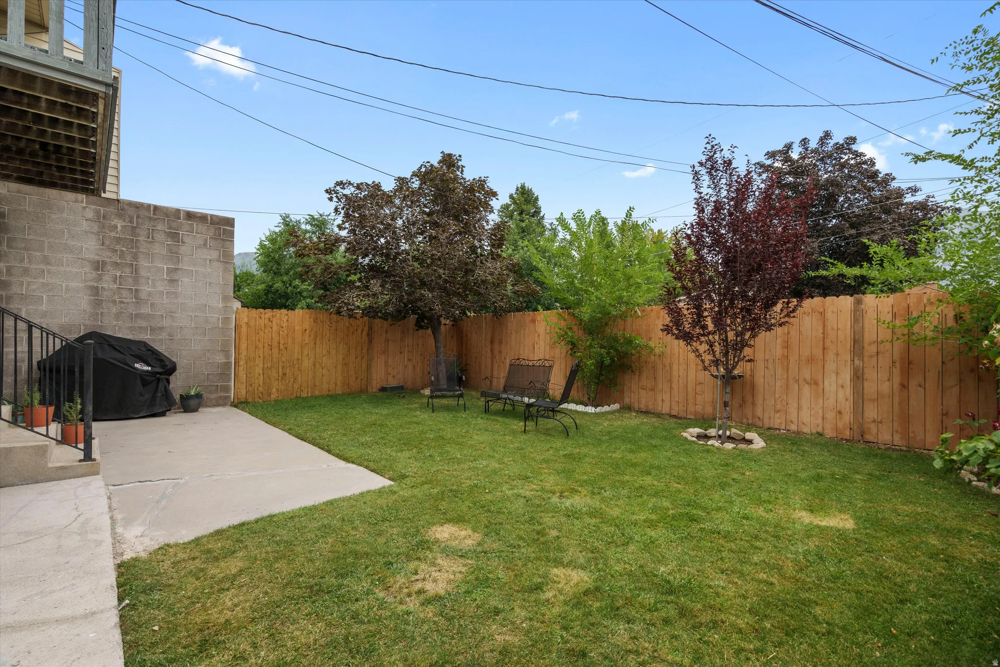 Expansive grassy yard featuring a private wood fence, mature trees, a concrete patio, and a block wall perimeter