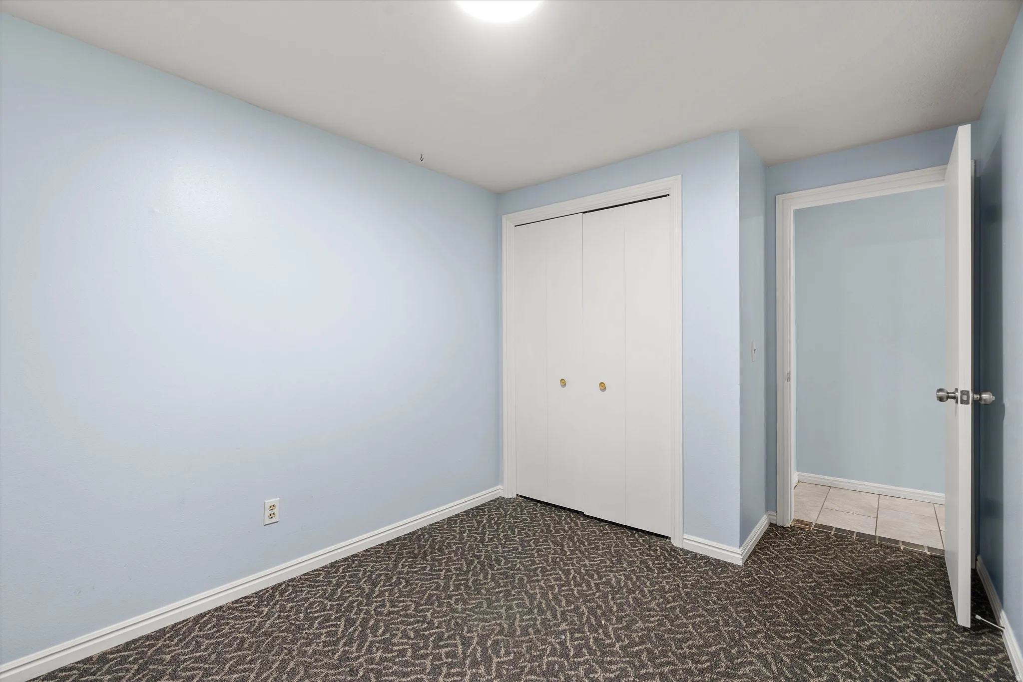 Room featuring patterned carpet flooring, light blue wall paint, white baseboards, and a flush mount ceiling light