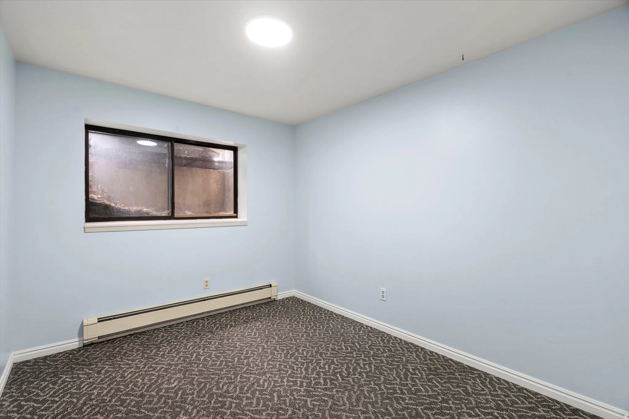 Room featuring light blue walls, a rectangular window with dark framing, white baseboards, and patterned carpet flooring