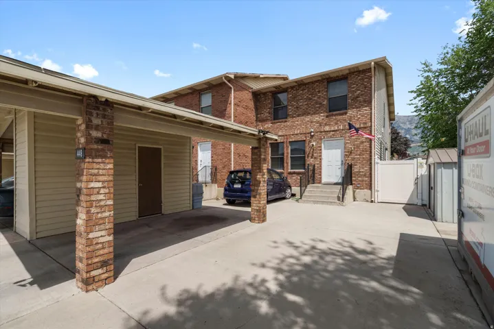 Brick exterior with tan siding features a carport, concrete driveway, and a white gate