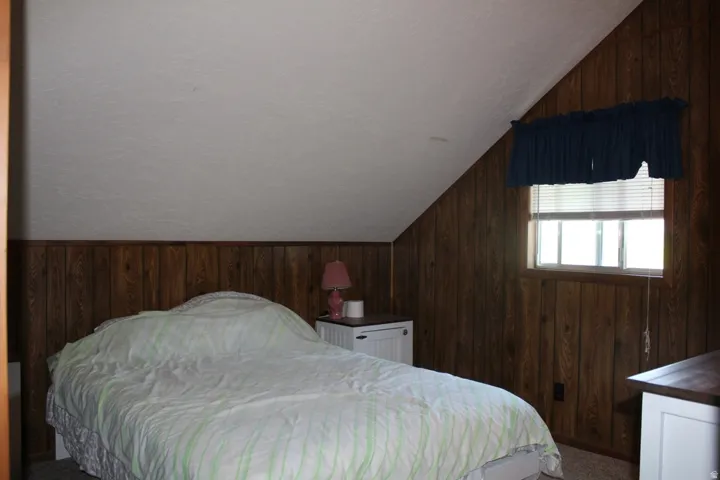 Bedroom featuring wood-finish paneling, a sloped white ceiling, and a window with blinds