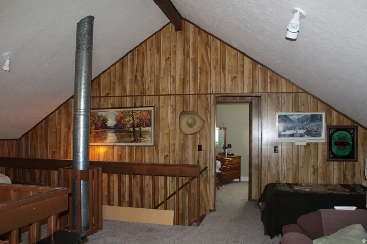 Vaulted ceiling space featuring wood-finish wall paneling, a metal vent pipe enclosure, and a built-in wood railing