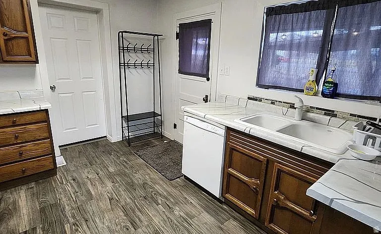 Kitchen featuring wood-finish flooring, white paneled doors, dual-basin sink, laminate countertops, and a tiled backsplash
