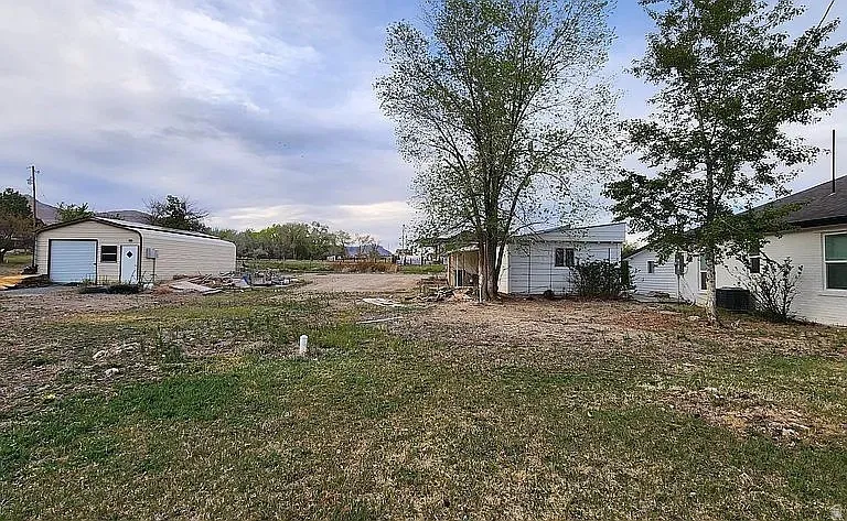 Expansive lot featuring a detached garage with an overhead door, multiple mature trees, and visible residential structures