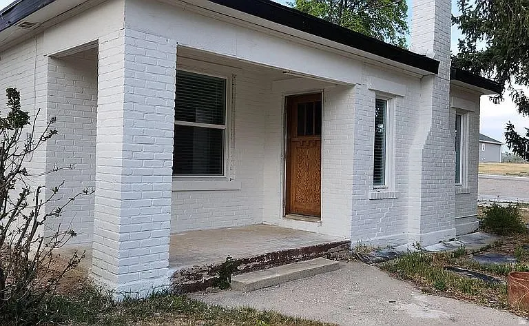 Brick exterior with white paint, covered entryway, wood-paneled front door, and multiple windows