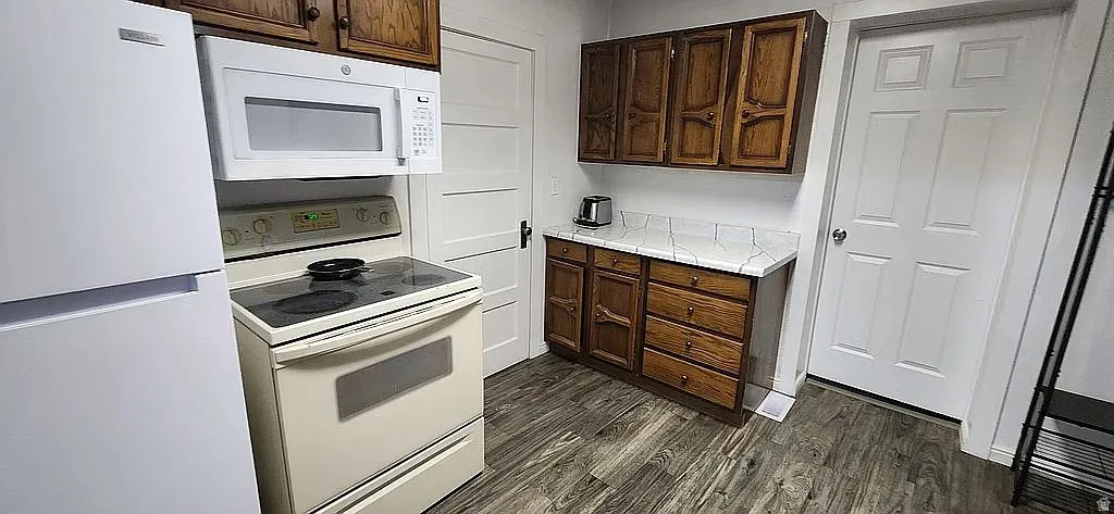 Kitchen featuring wood-finish flooring, white appliances, and wood cabinetry