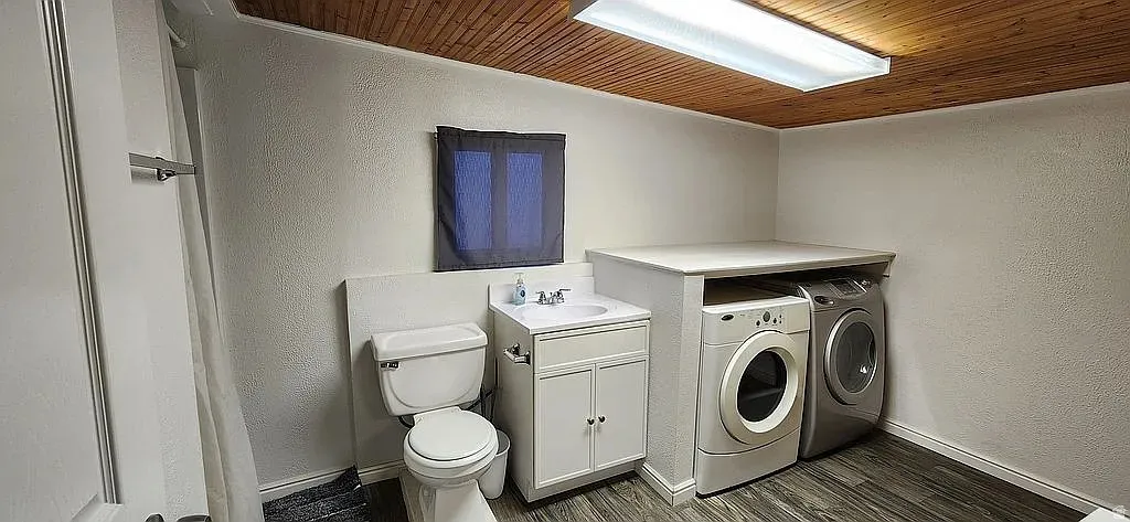 Functional laundry and utility area featuring a wood-finish ceiling, wood-finish flooring, a white vanity with integrated sink, and a white toilet