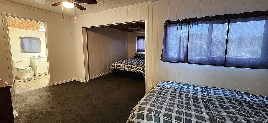 Carpeted interior space featuring white paneled walls, a ceiling fan with integrated lighting, and a doorway to a bathroom with a white vanity and toilet